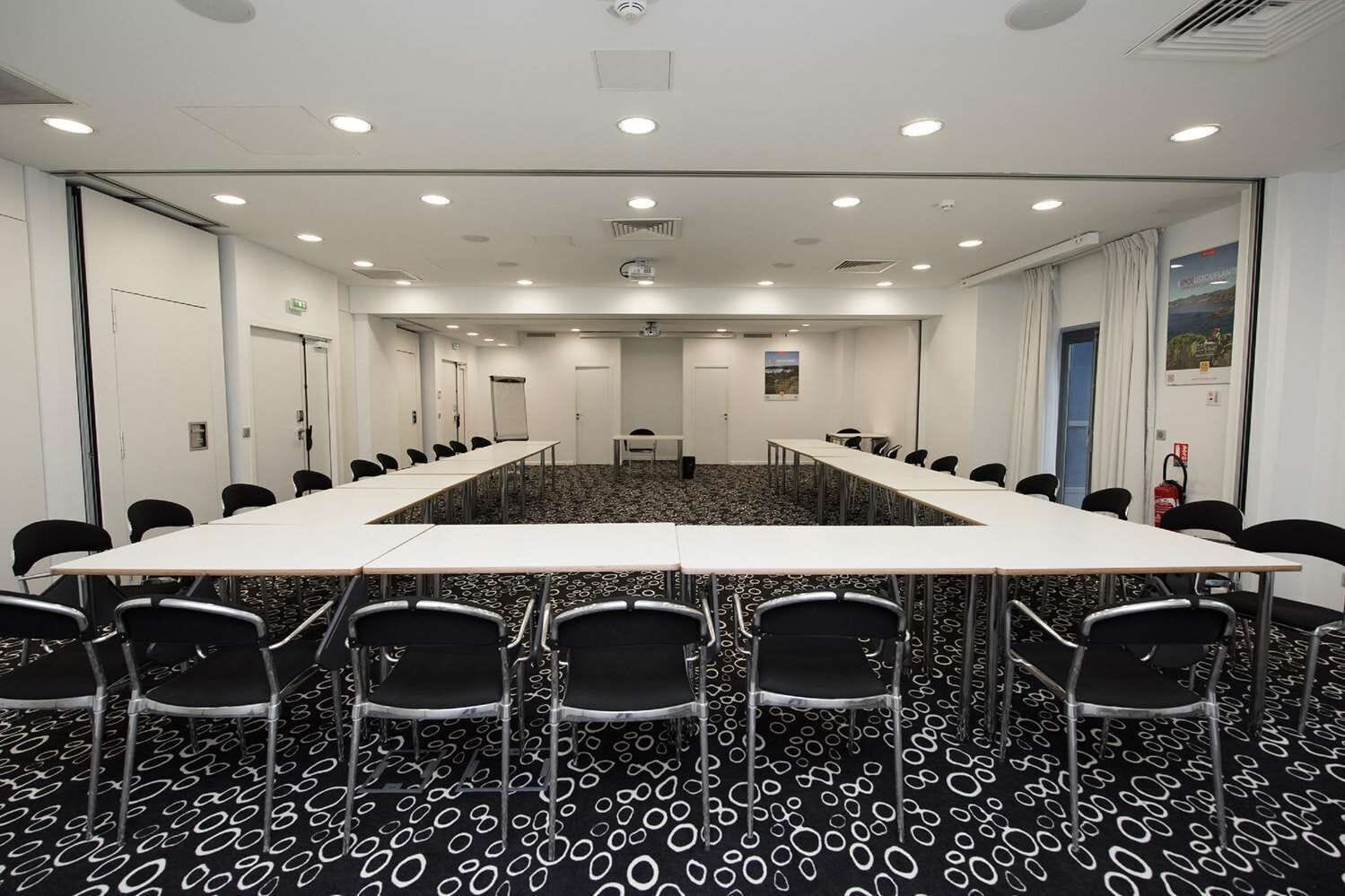 A conference room with a long table, black chairs, a patterned carpet, and white walls.