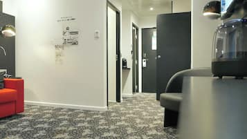 A modern hotel lobby with a patterned carpet, a red seating area, a reception desk, and a television screen.