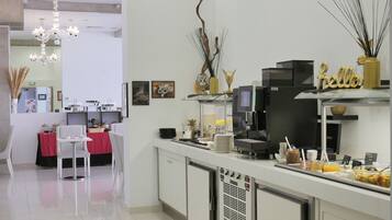 Un caffè moderno con un design pulito e minimalista, che include una macchina per il caffè, un banco buffet con diversi prodotti alimentari e un'area salotto con una tovaglia rossa.