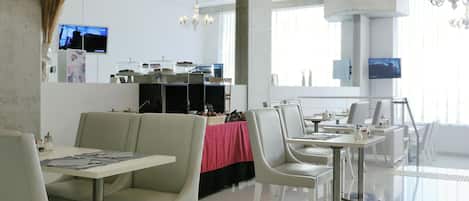 Un restaurante moderno con mobiliario blanco, un mantel rojo y un televisor en la pared.