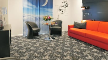 A modern living room with a black and white patterned carpet, a red sofa, two black chairs, a small round table with a flower vase, and a wall with a moon and stars mural.