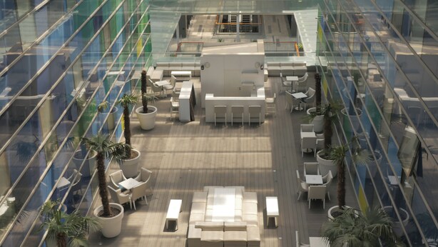 Un moderno atrio interior con una zona de estar central, rodeado de paredes de vidrio y plantas en macetas.