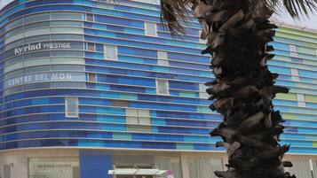 Un edificio moderno con fachada azul y el nombre 'Kyriad Prestige Centre Del Mon' a la vista.