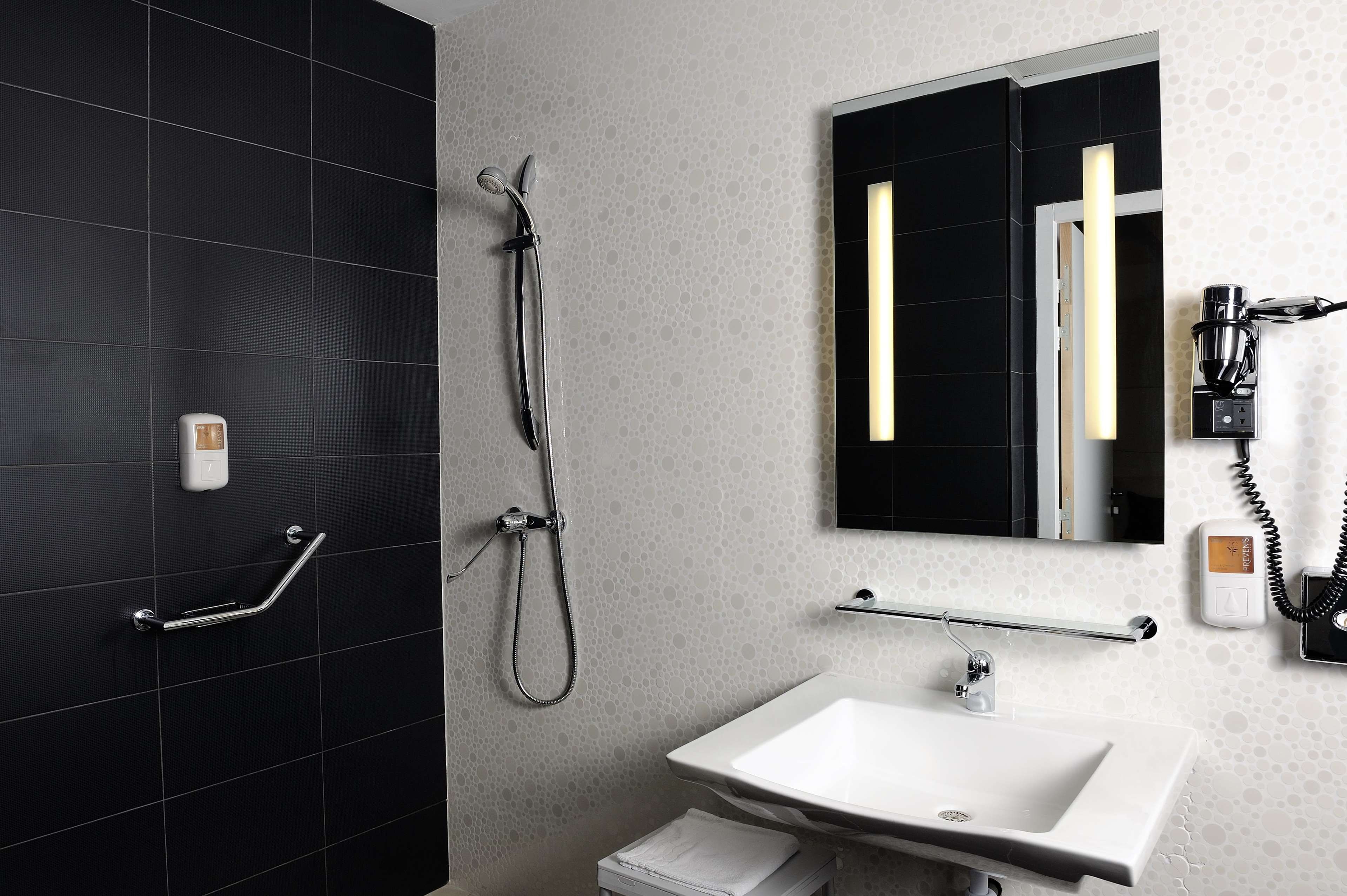 Un baño moderno con ducha de azulejos negros, lavabo blanco y espejo con marco negro.