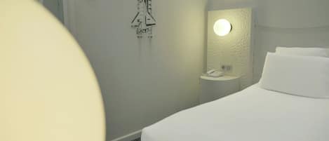 Habitación de hotel con cama, mesita de noche con teléfono, luz empotrada en la pared y una decoración con transbordador espacial.