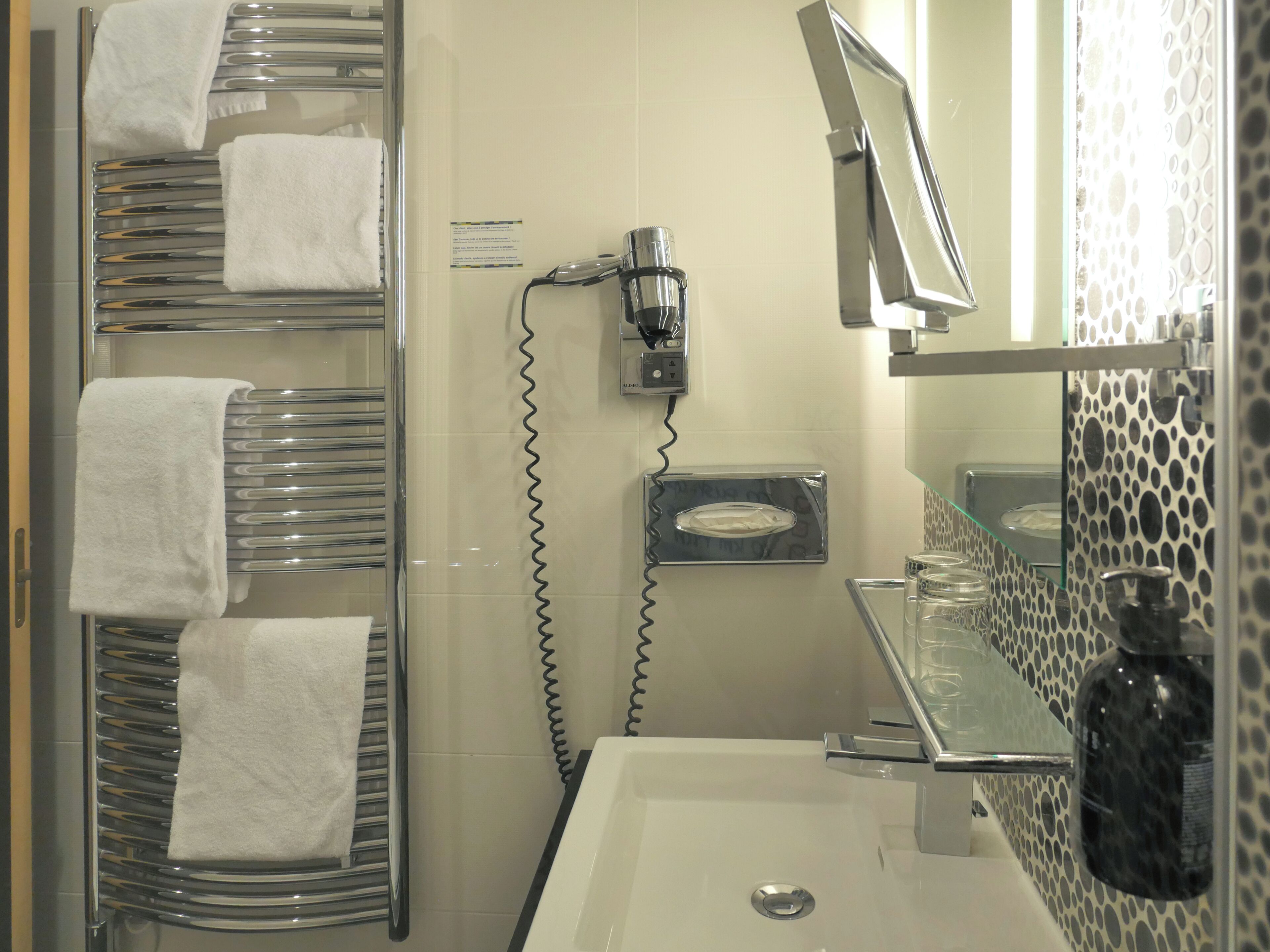 A bathroom with a glass shower enclosure, a white sink, a mirror, and a towel rack with multiple towels.