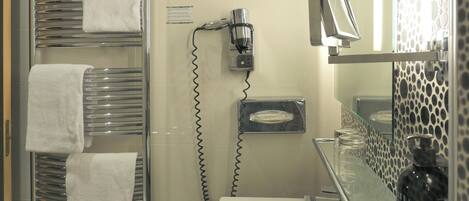 A bathroom with a glass shower enclosure, a white sink, a mirror, and a towel rack with multiple towels.