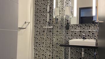 A modern bathroom with a glass-enclosed shower, a white sink, and a patterned wall.