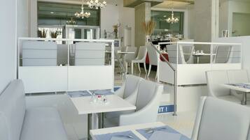 Um restaurante moderno com móveis brancos, um lustre e um painel de vidro separando a área de jantar da cozinha.
