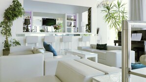 Una sala de estar moderna con sofás blancos, un televisor de pantalla plana y una zona de bar con estantes y plantas.
