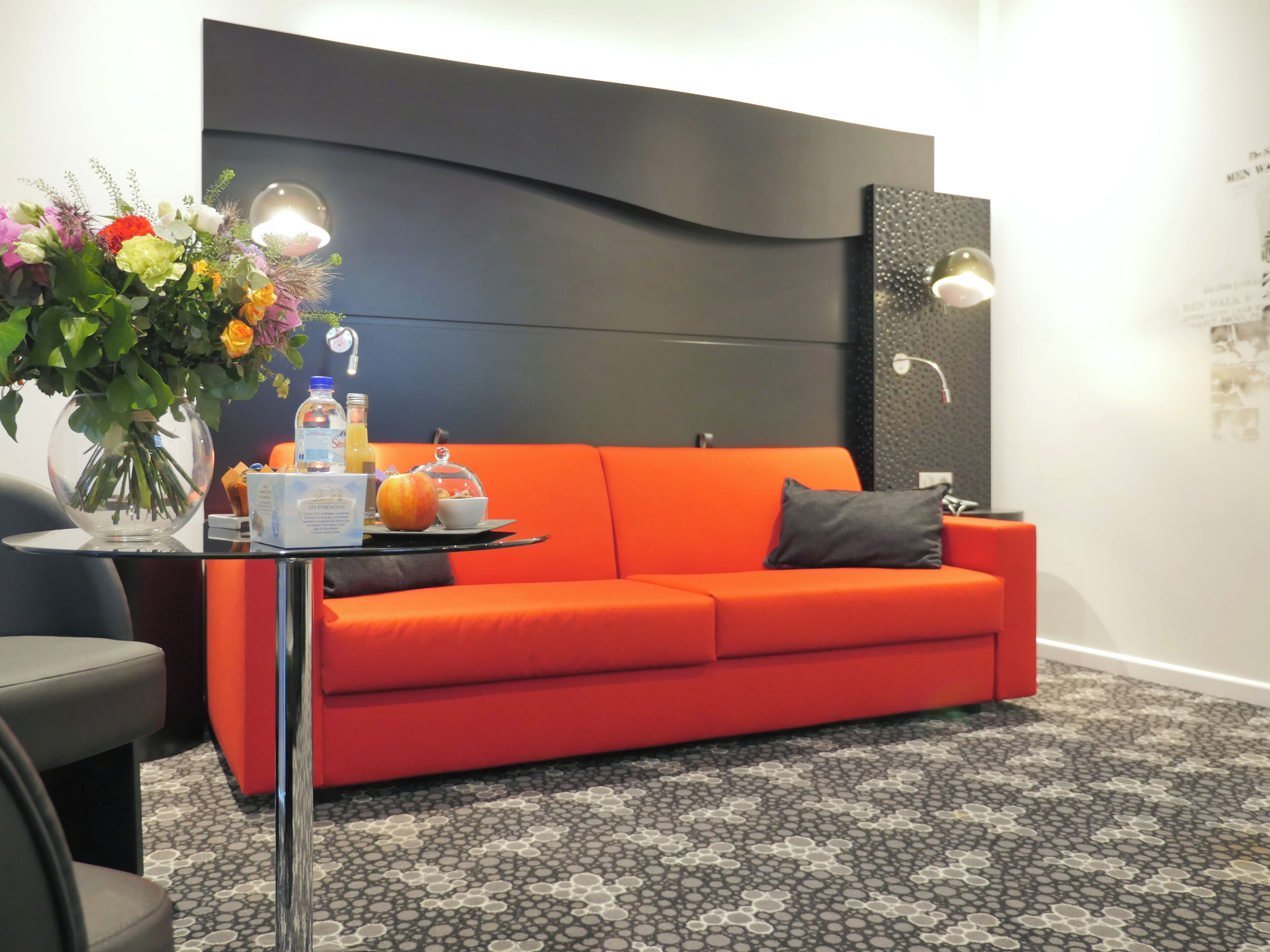 Ein modernes Zimmer mit einem roten Sofa, einer Glasvase mit Blumen und einem Tablett mit Frühstücksgebäck.