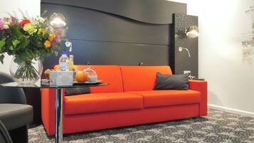 Ein modernes Zimmer mit einem roten Sofa, einer Glasvase mit Blumen und einem Tablett mit Frühstücksgebäck.