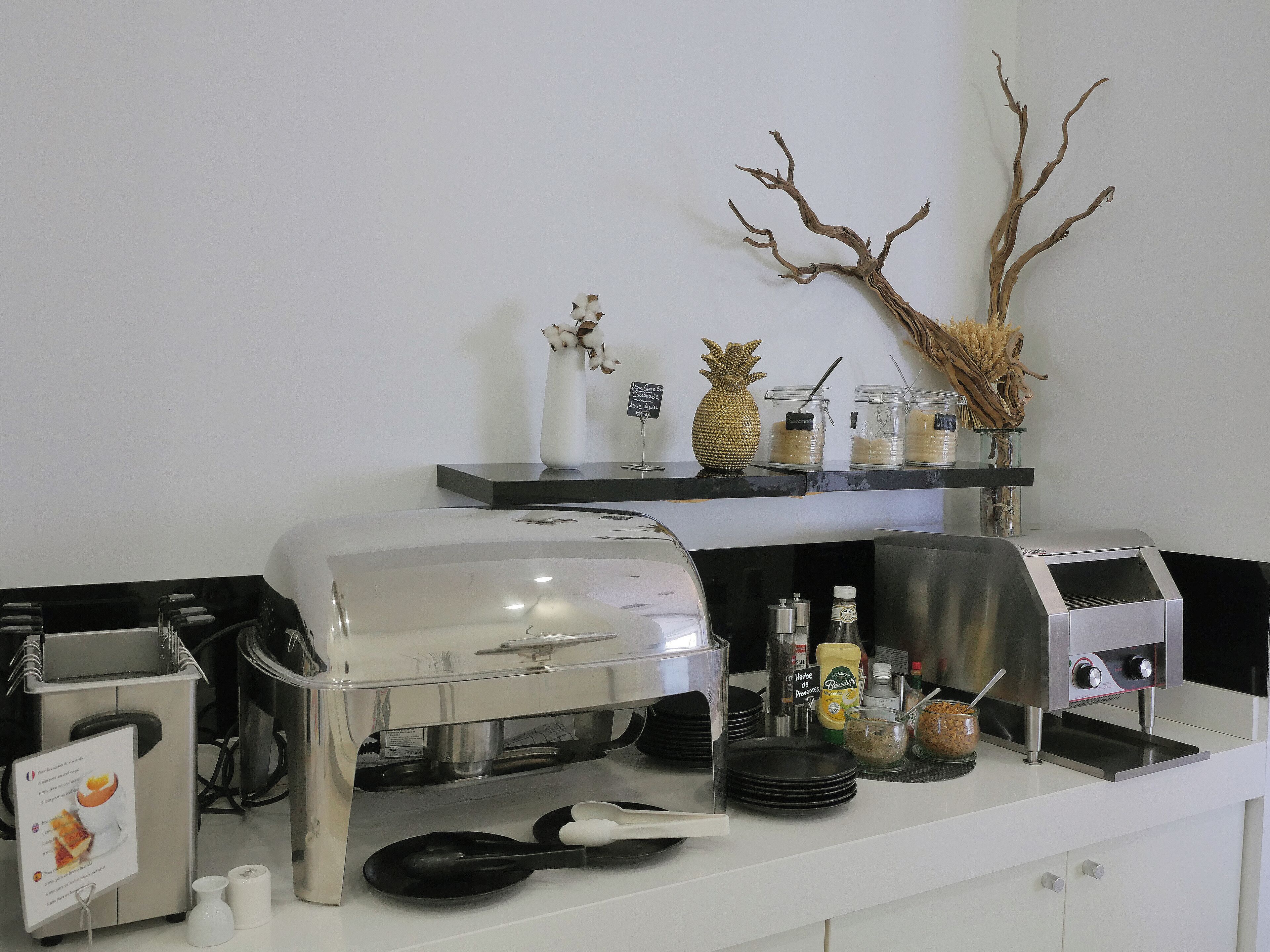 Een keukenhoek met een koffieapparaat, een broodrooster en een buffet met een ananas en decoratieve takken.