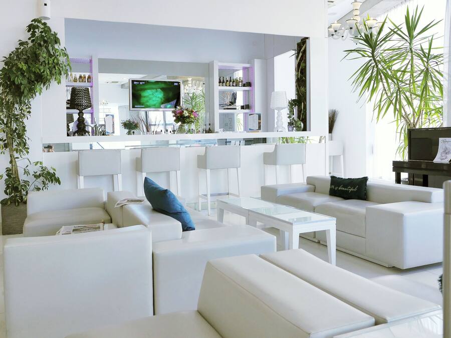 A modern living room with white sofas, a flat-screen TV, and a piano.