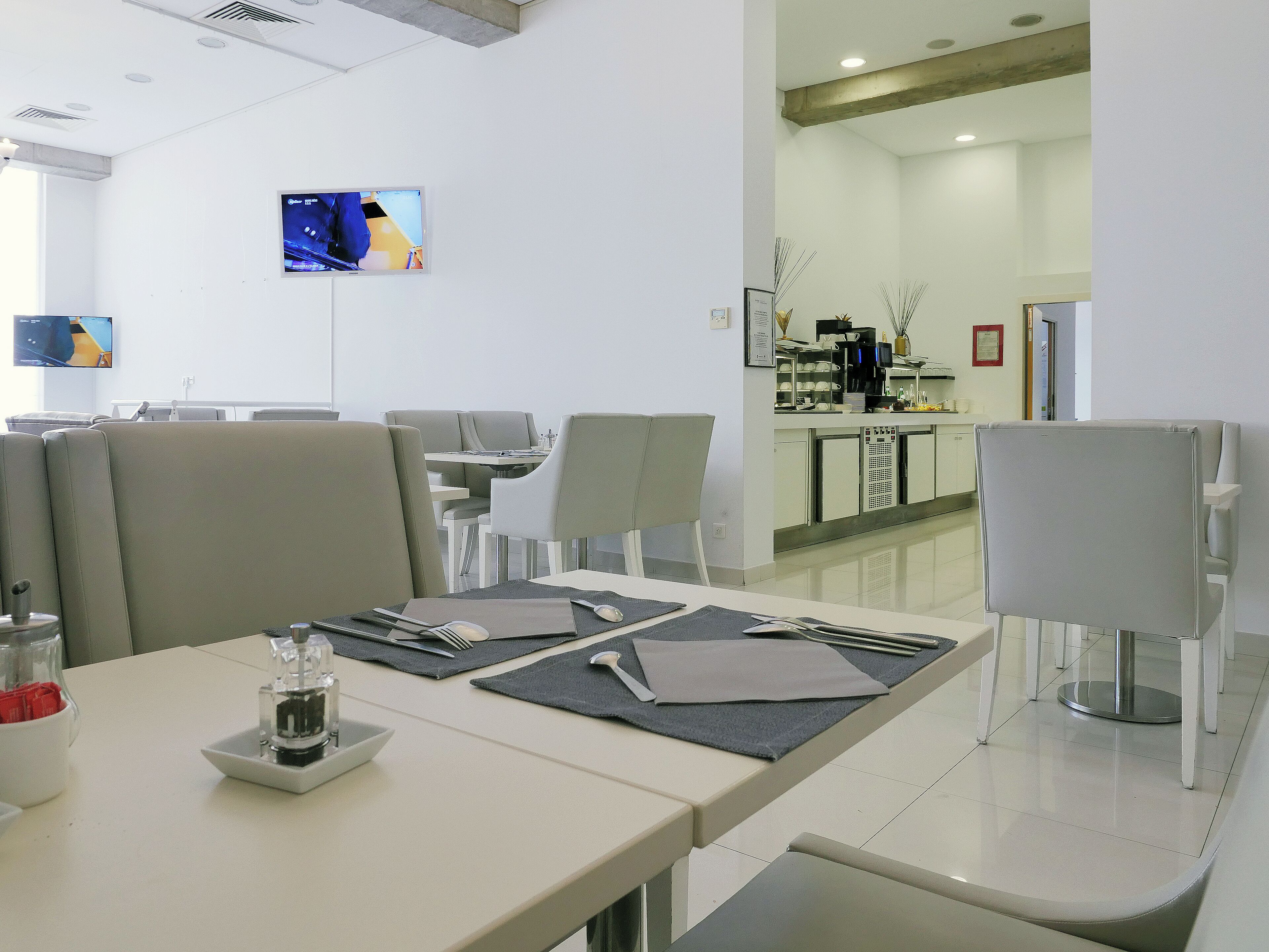 Un espace repas moderne avec des tables prévues pour deux personnes, une machine à café et un téléviseur fixé au mur.