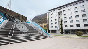 A modern hotel with a staircase leading to the entrance, a clear view of the surrounding buildings, and a mountainous backdrop.
