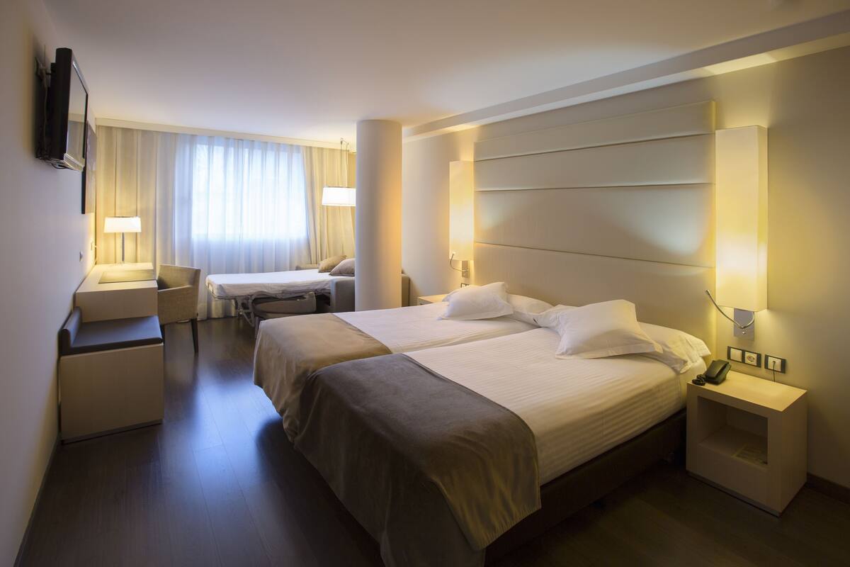 Une chambre d’hôtel avec deux lits, un bureau, une chaise, une télévision et une lampe.