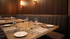 A dining area with wooden panel walls, recessed lighting, and a booth seating arrangement.