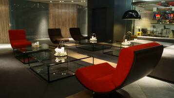 A modern lobby with glass coffee tables, red and black chairs, and a bar area with glass shelving.