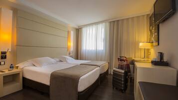 Ein Hotelzimmer mit zwei Betten, einem Schreibtisch, einem Stuhl, einem Koffer und einem Fernseher an der Wand.