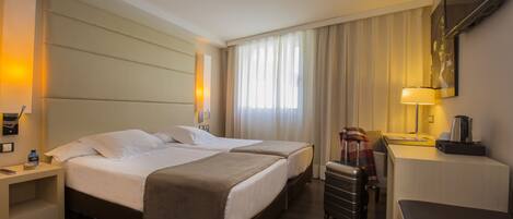 Ein Hotelzimmer mit zwei Betten, einem Schreibtisch, einem Stuhl, einem Koffer und einem Fernseher an der Wand.