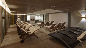 Uma sala de conferências moderna com fileiras de cadeiras e uma mesa comprida, piso de madeira e iluminação embutida.