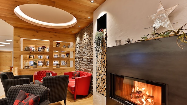 Uma sala de estar moderna com lareira, prateleiras de madeira e poltronas estofadas em vermelho e cinza.