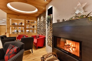 A modern living room with a fireplace, wooden shelves, and red and grey upholstered chairs. - Hotel Zum Mohren (Reutte)