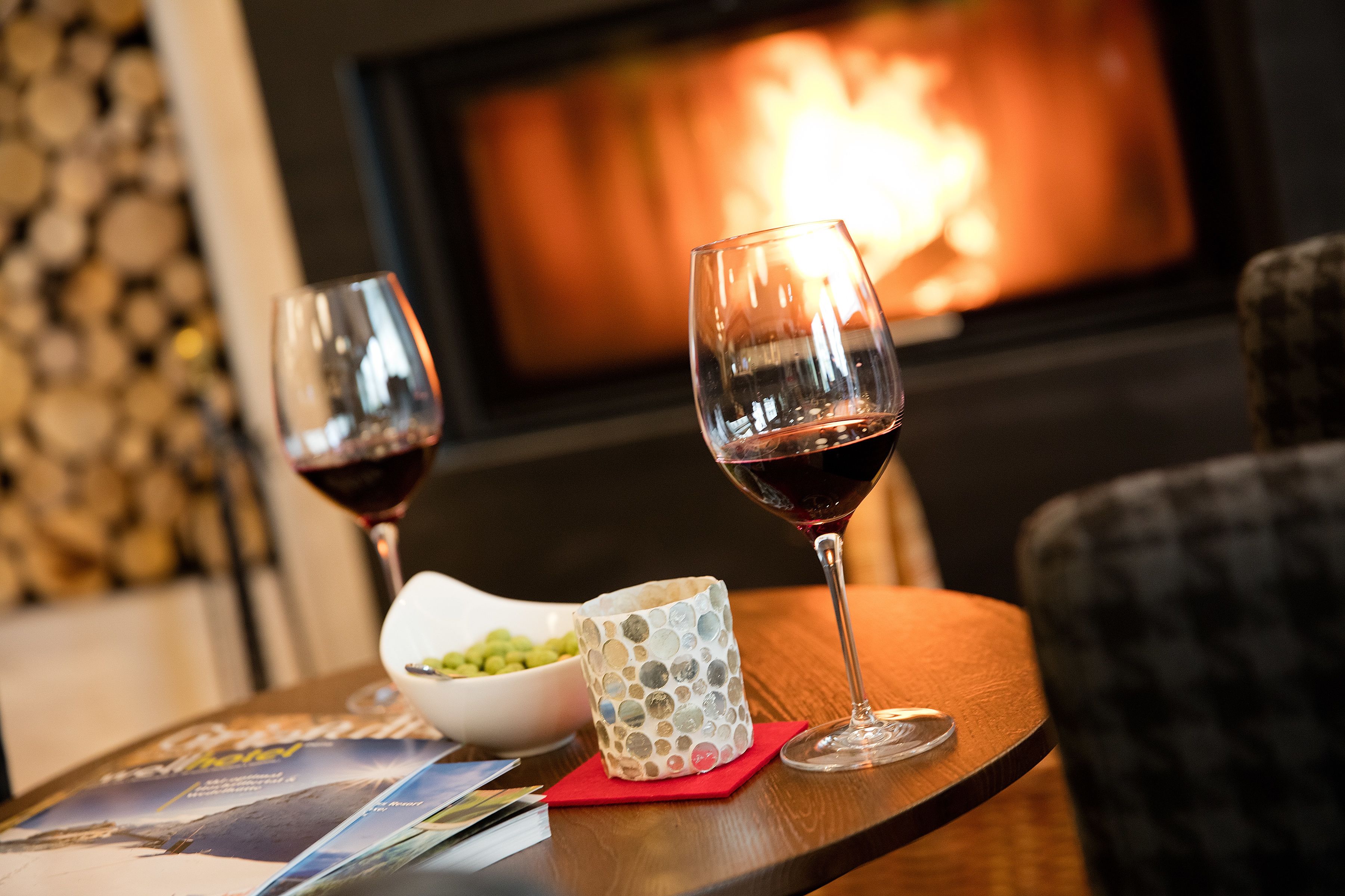 A table with two wine glasses and a decorative bowl, set against a backdrop of a fireplace and a television screen.