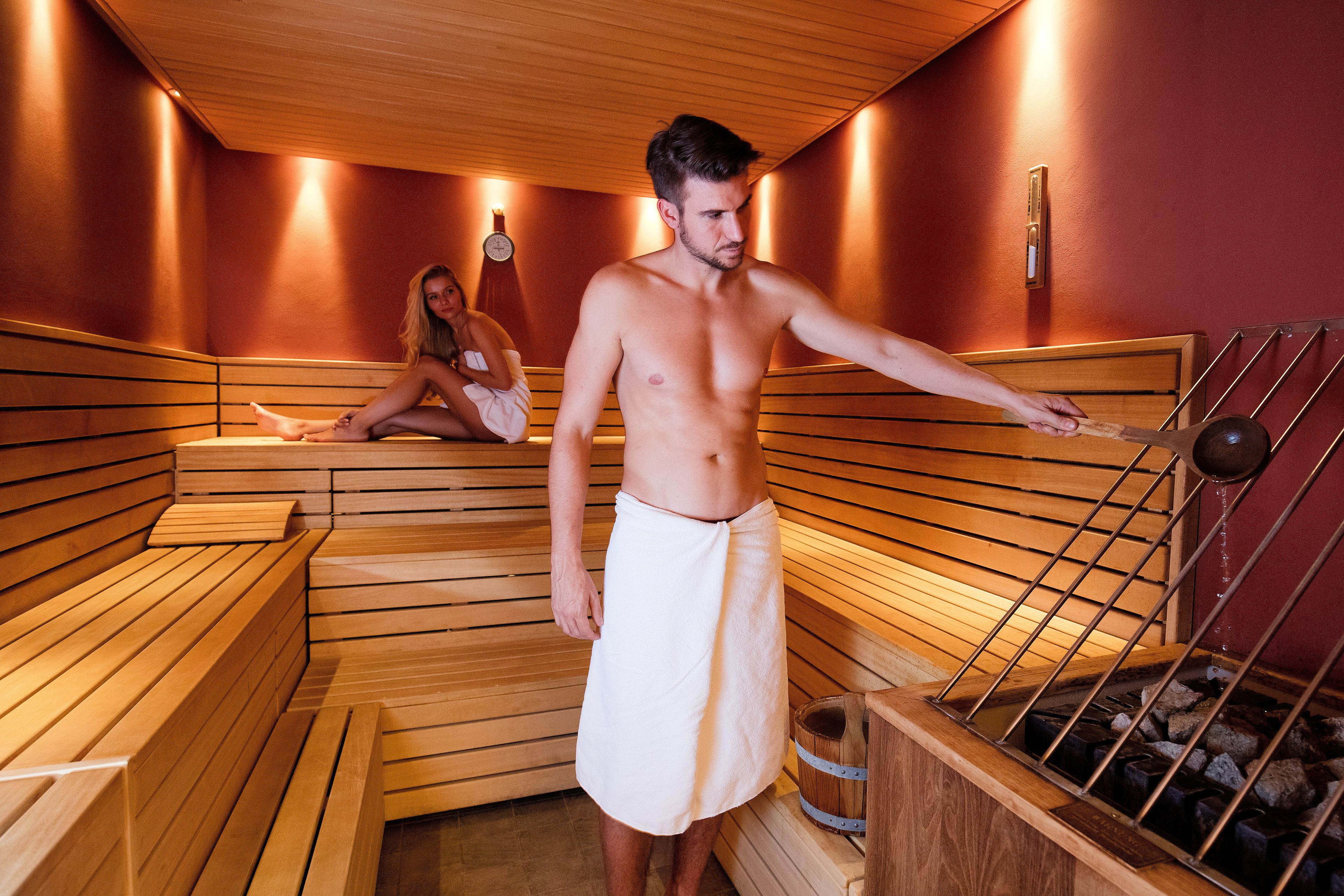 Un sauna avec des bancs en bois et une personne utilisant un outil en bois.