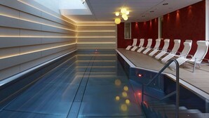 Uma área interna de piscina moderna com piso de vidro, cadeiras de lounge brancas e claraboia.