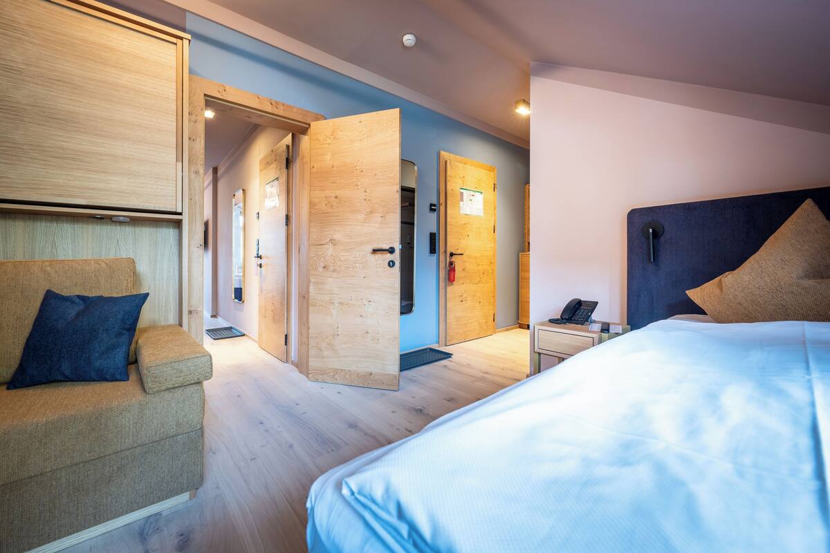 Ein Hotelzimmer mit einem Bett, einem Sofa und einer Holztür zu einem anderen Raum.