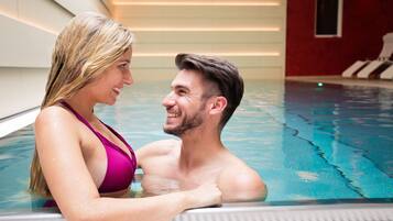 Una pareja en una piscina con suelo de baldosas y una pared roja al fondo.