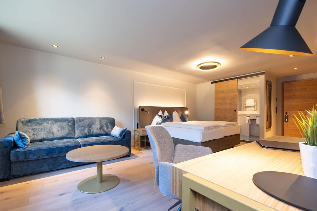 Ein modernes Hotelzimmer mit einer Couch, einem runden Tisch, einem Bett und einem Schreibtisch mit Stuhl.