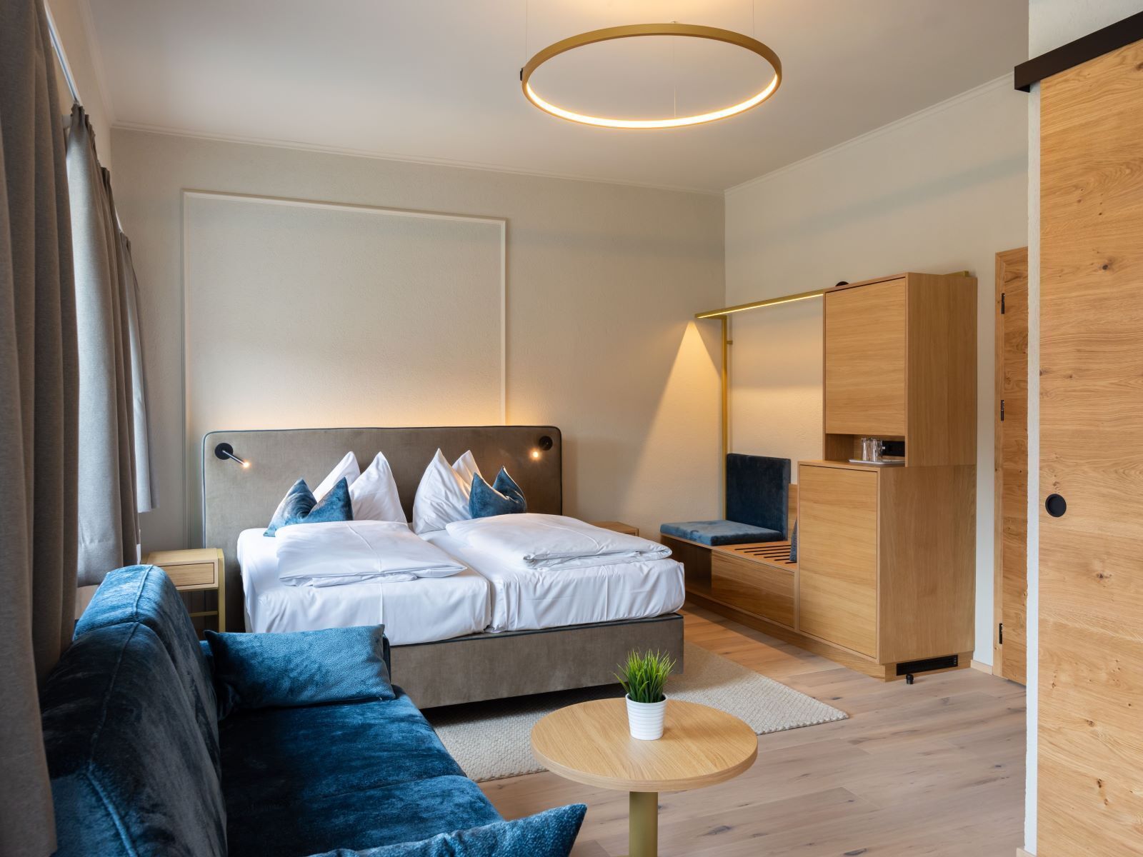 A modern bedroom with a bed, a sofa, a small table with a plant, and a wardrobe.