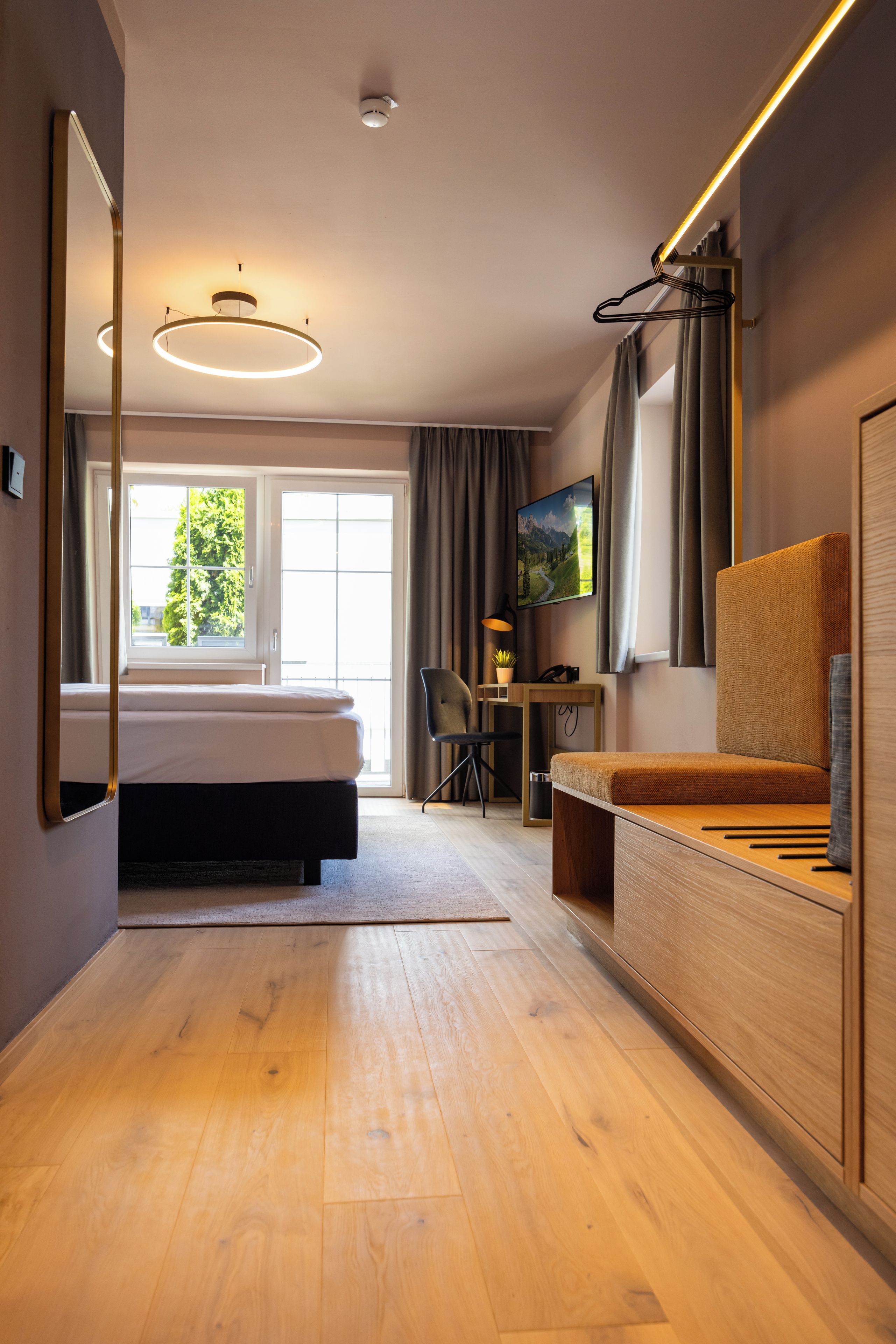 Een moderne hotelkamer met een bed, een bureau, een stoel, een televisie en een grote spiegel.