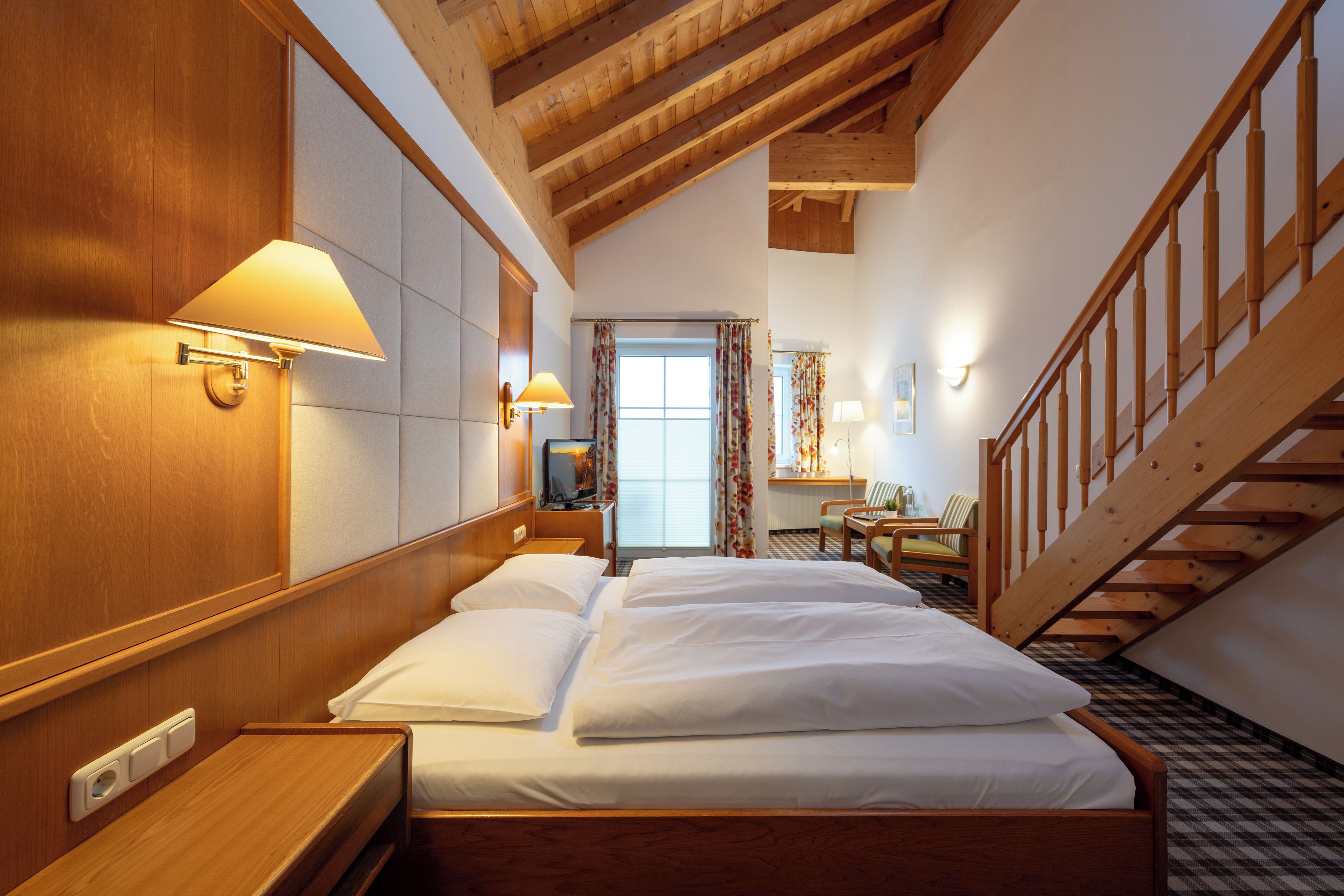 Ein Hotelzimmer mit einem hölzernen Bett, einem Schreibtisch, einem Stuhl, einem kleinen Tisch und einer Treppe.