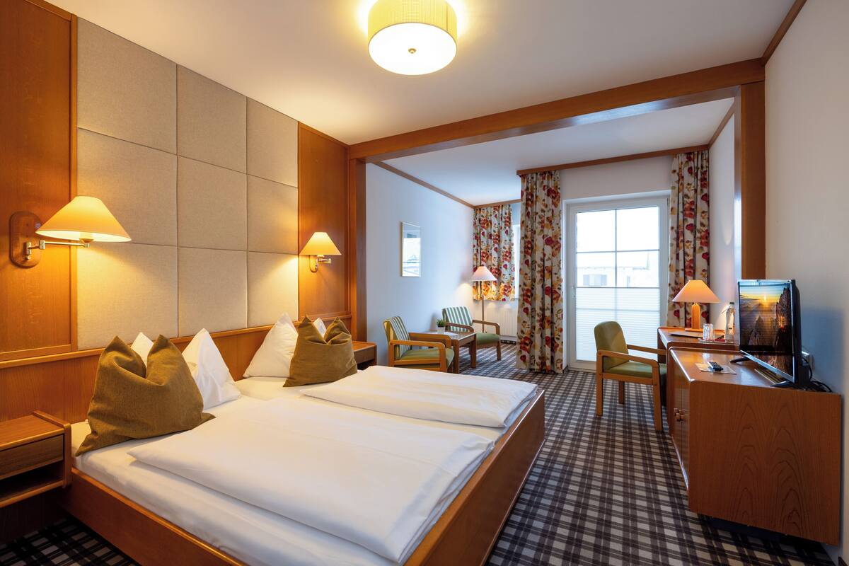 Ein Hotelzimmer mit einem großen Bett, zwei Nachttischlampen, einem Schreibtisch mit Fernseher und einem Sessel.