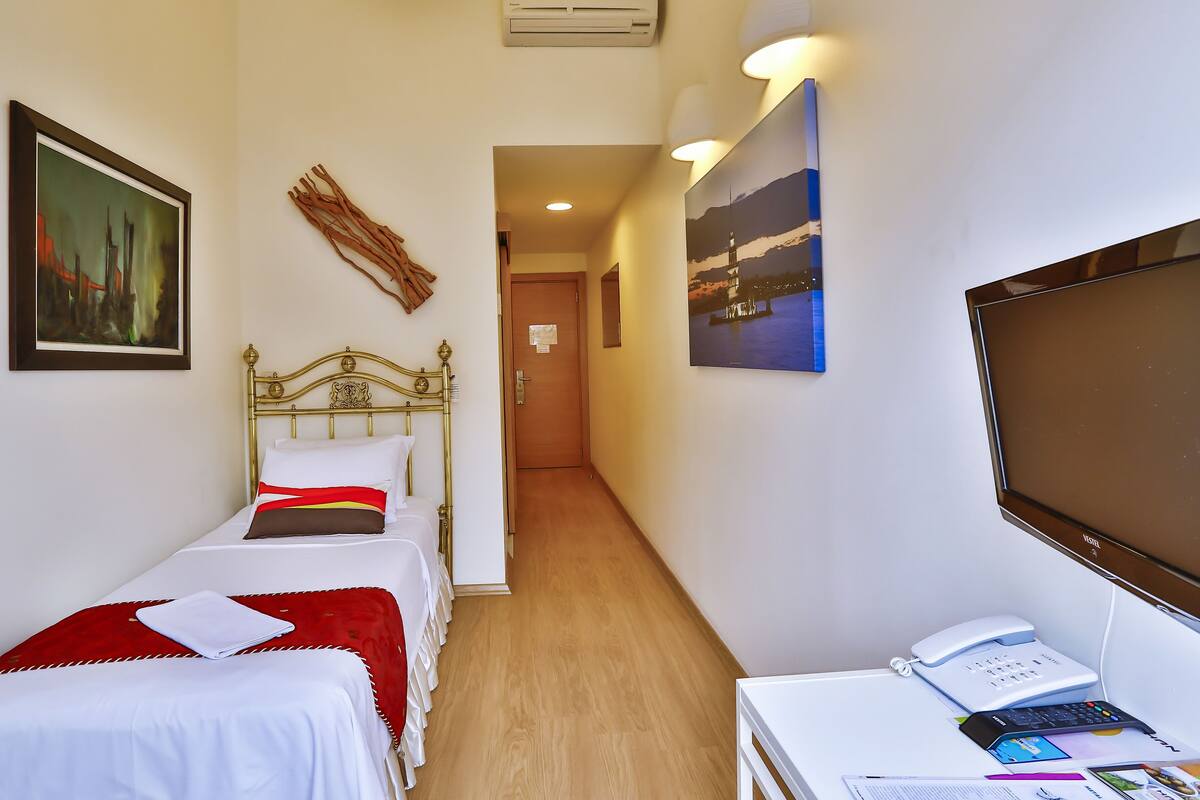 A hotel room with two single beds, a desk with a phone and a laptop, a TV, and artwork on the walls.