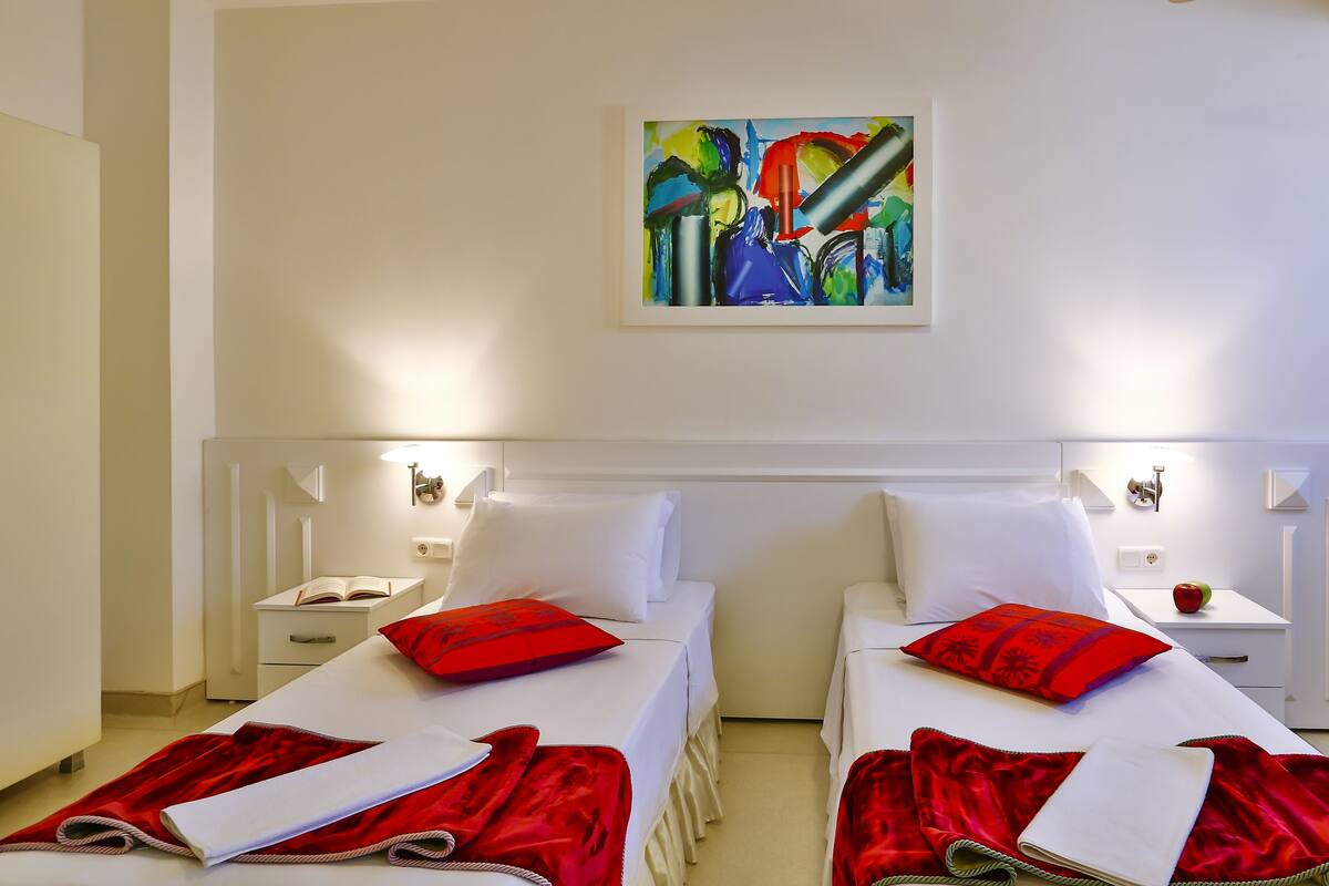 A hotel room with two beds, each with red pillows and a red blanket. There is a painting on the wall above the beds.