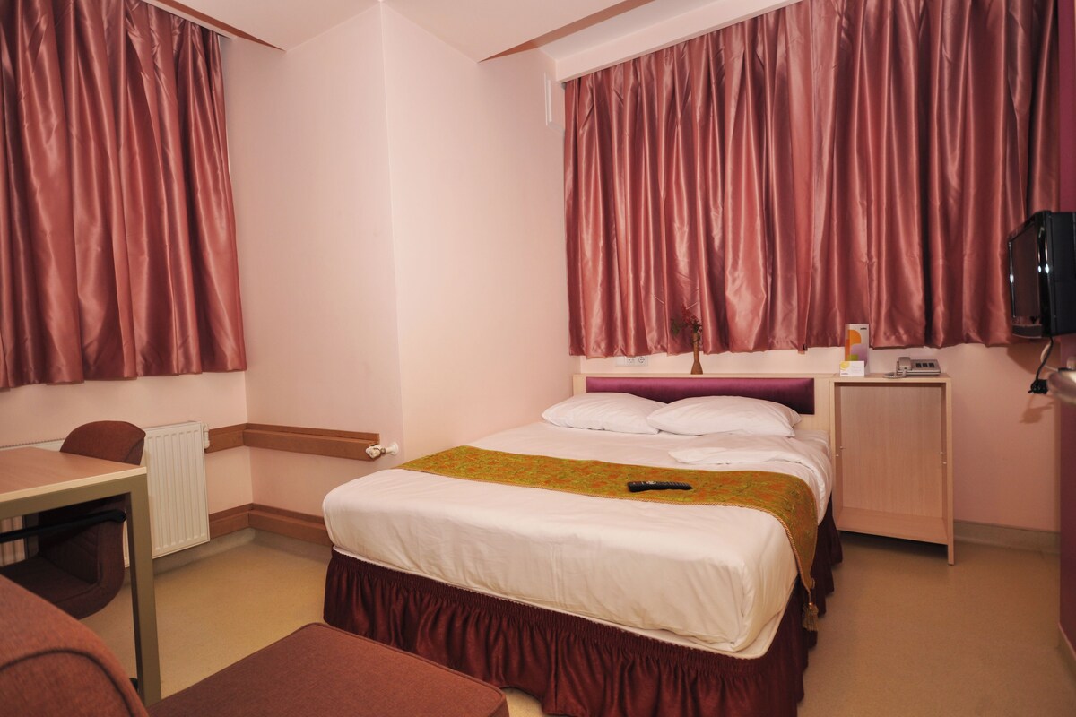 A hotel room with a bed, a desk, a chair, a TV, and a wardrobe.