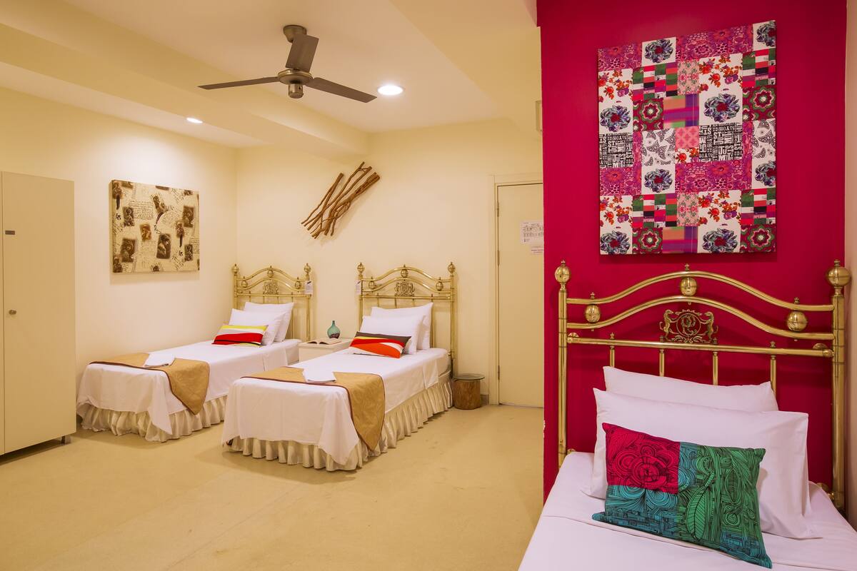 A hotel room with two single beds, a ceiling fan, a quilted wall hanging, and a red accent wall.