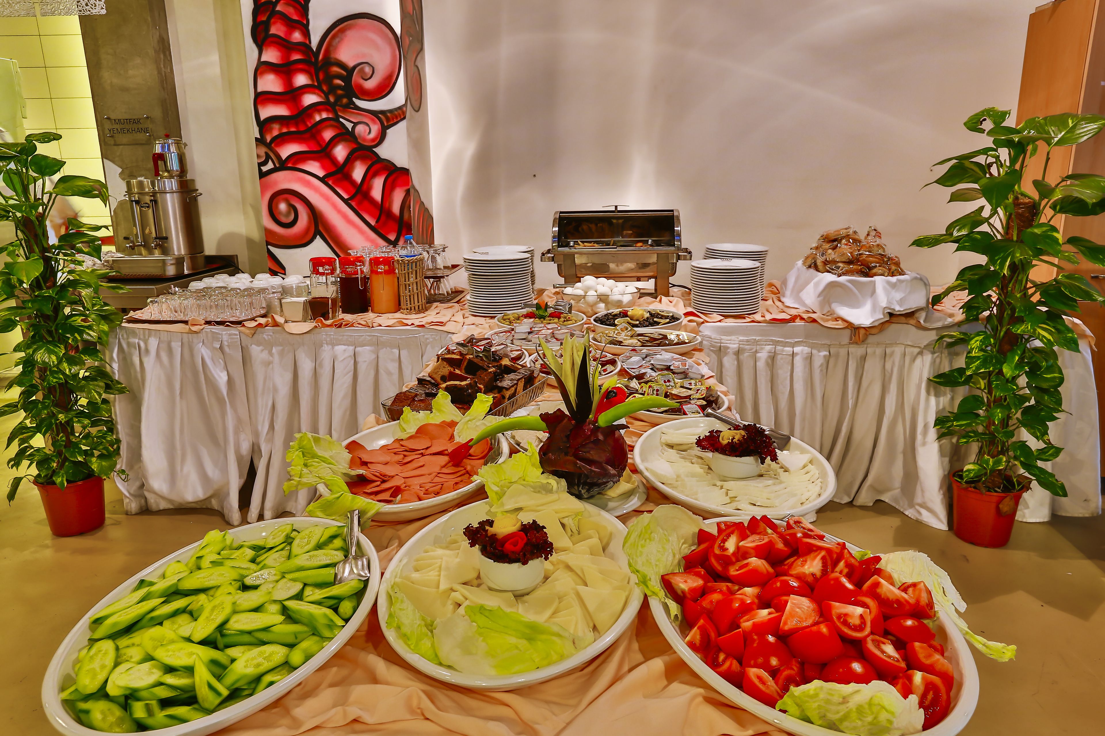 A buffet table with various food items, including vegetables, salads, and meats, set against a backdrop with a large abstract painting.