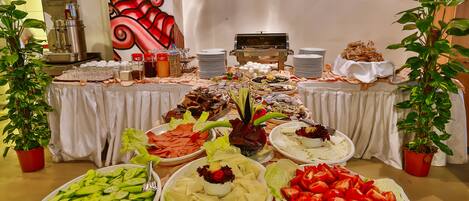 A buffet table with various food items, including vegetables, salads, and meats, set against a backdrop with a large abstract painting.