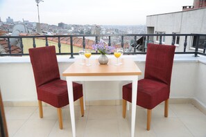 A balcony with two red chairs, a wooden table, and two glasses of orange juice.