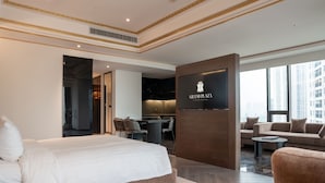 Une chambre d’hôtel avec un grand lit, un canapé, un bureau et un téléviseur diffusant l’émission « Grand Plaza ».