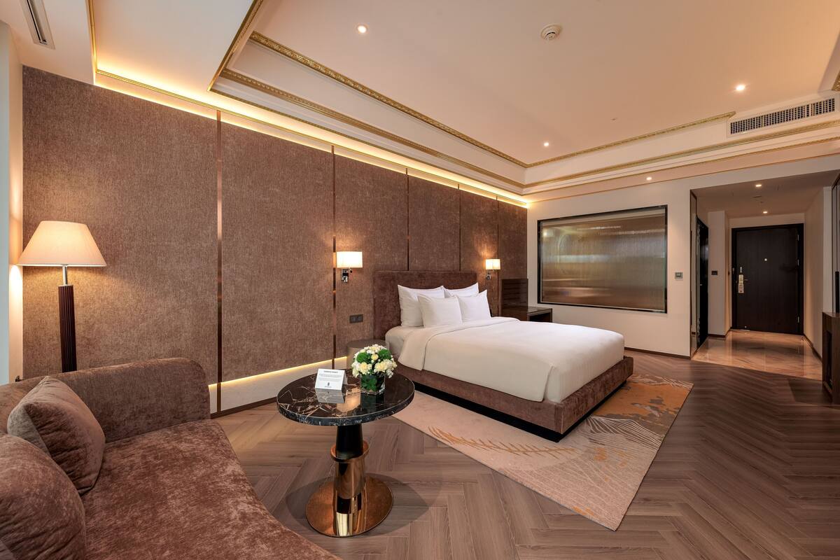 Een moderne hotelkamer met een groot bed, een bank, een ronde tafel en een aan de muur bevestigde televisie.