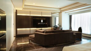 Een moderne hotelkamer met een groot flatscreen-televisie, een bank, een bureau met een stoel en een groot raam.