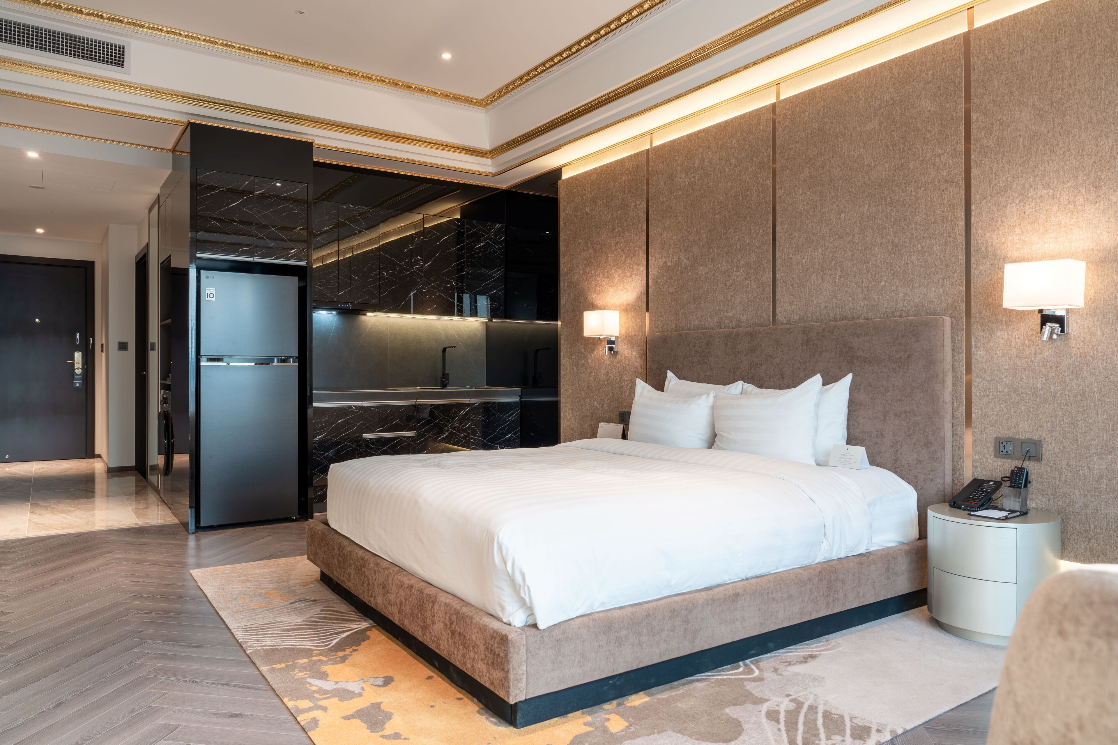 A modern hotel room with a large bed, a built-in kitchen, and a separate bathroom.