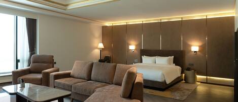 Una habitación de hotel con una cama grande, dos sillones, un sofá, una mesita y lámparas de pared.